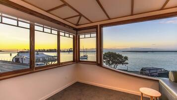 A corner room with a view of a waterfront, a small wooden stool, and a leather couch.