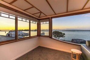 A corner room with a view of a waterfront, a small wooden stool, and a leather couch.