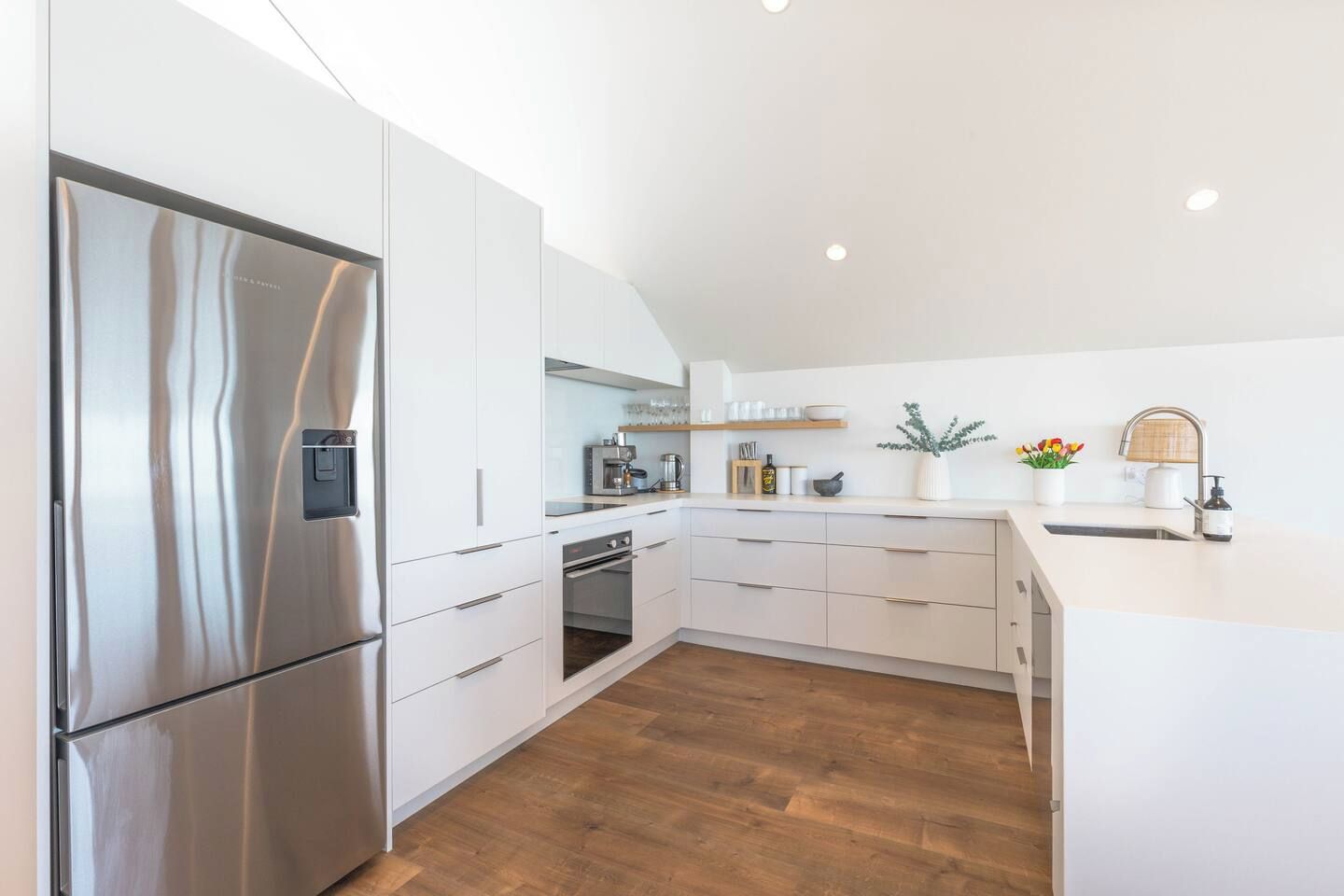 A modern kitchen with white cabinetry, stainless steel appliances, and a wooden floor.