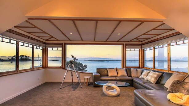 Ein Zimmer mit großem Fenster mit Blick auf ein Gewässer, einem Teleskop, einer Ledersofa und einem Glastisch.