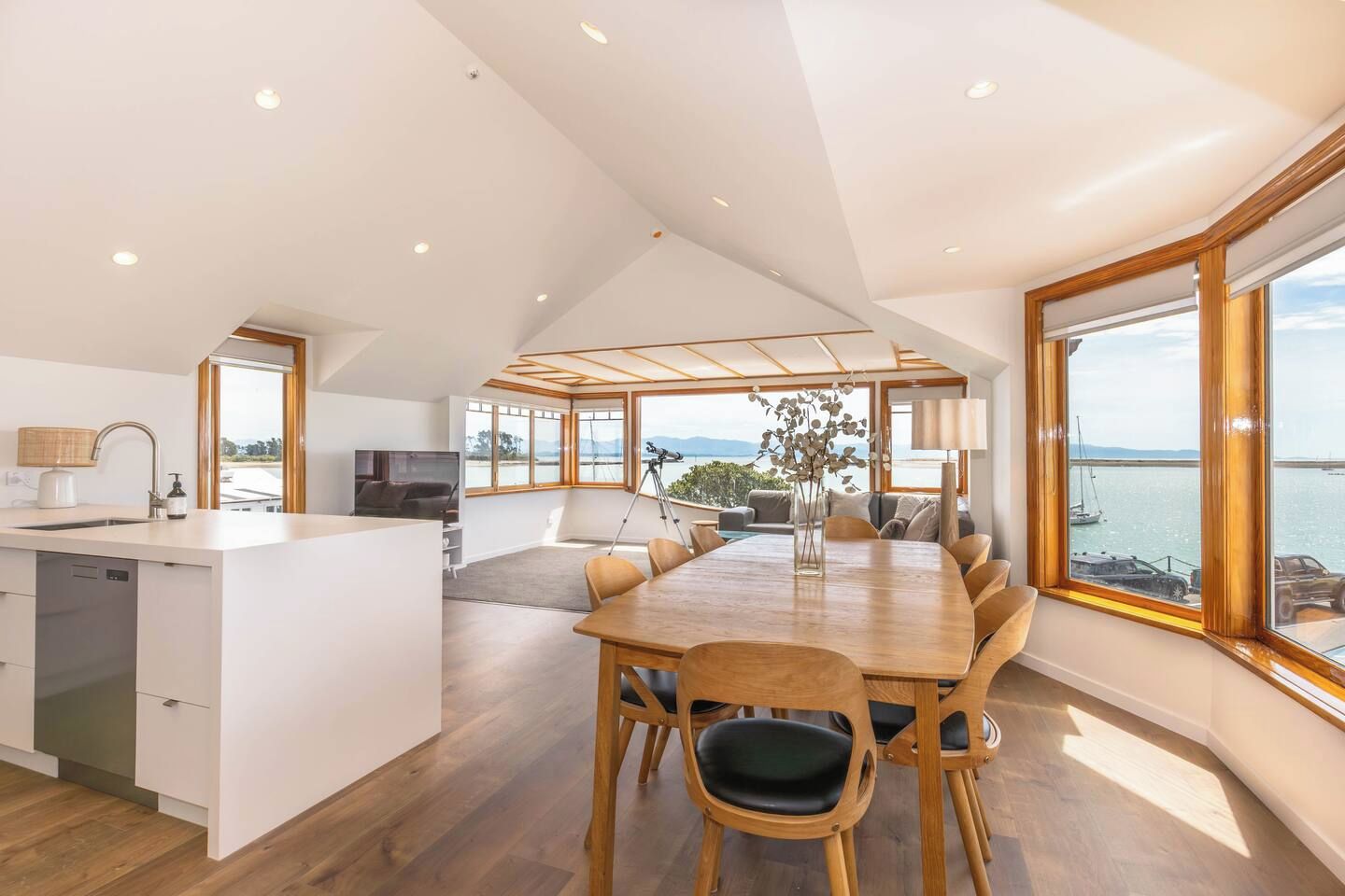 Une cuisine spacieuse dotée d’un îlot central, un coin repas avec une grande table et une vue sur la mer grâce à de larges fenêtres.