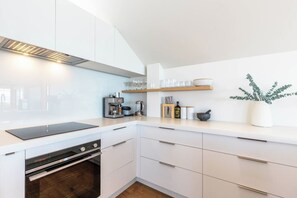 A modern kitchen with white cabinetry, a built-in oven, a coffee machine, and a plant on the counter.