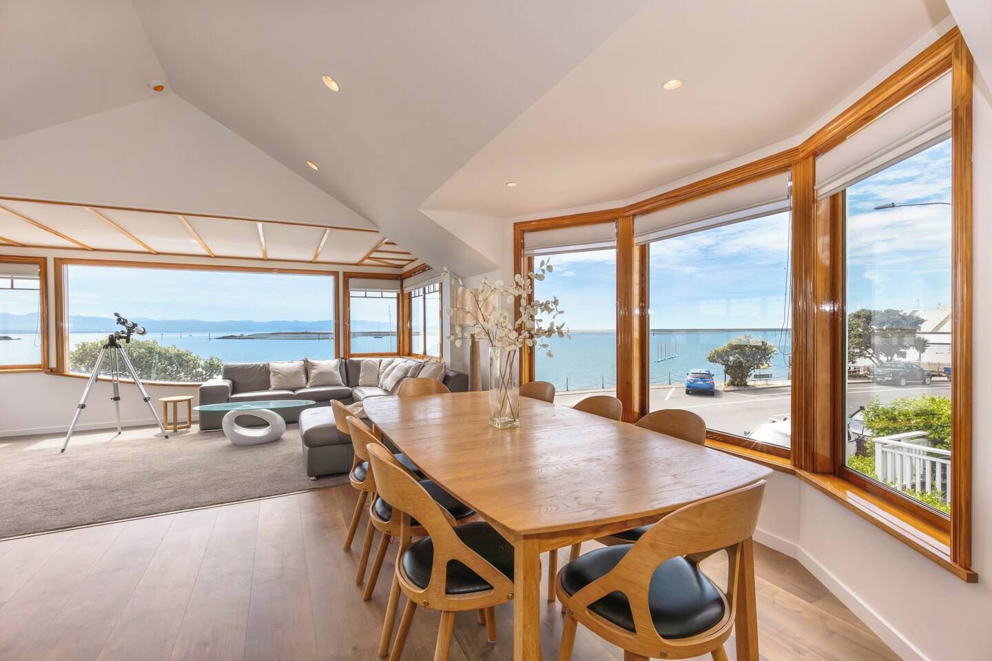 A spacious room with a large wooden dining table, comfortable seating, and a view of the sea.