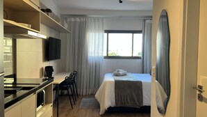 A hotel room with a bed, a desk with a chair, a television, and a large window with curtains. - Vrbo Property (São Paulo)