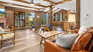 A spacious living area with wooden flooring, a fireplace, and large windows offering views of the outdoors. - Machins House Newly Remodled 4 bdrm backs up against RMNP (Estes Park)