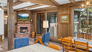 Una habitación acogedora con chimenea, paredes de madera, un ventanal grande y una mesa con sillas.