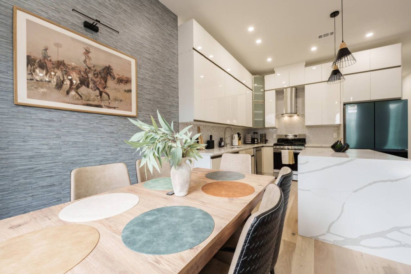 Una cocina moderna con armarios blancos, una campana extractora de acero inoxidable y un comedor con mesa y sillas de madera.