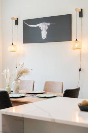 A dining area with a table set for four, two chairs, a vase with pampas grass, and a wall-mounted picture of a cow's head. - Weekend Getaway-Walk to Coffee Shop- 2 Car Garage! (Nashville)