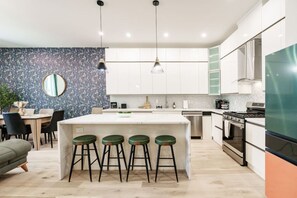 A modern kitchen with a central island, bar stools, and a dining area with a round table and chairs. - Getaway! Walk to Coffee and Food -2 Car Garage! (Nashville)