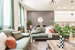 A modern living room with a sofa, a coffee table, and a dining area. - Getaway! Walk to Coffee and Food -2 Car Garage! (Nashville)