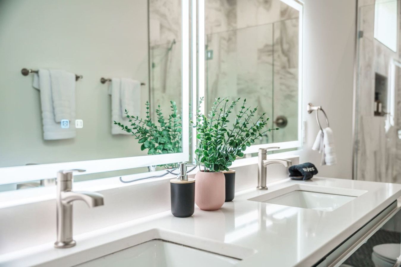 Un baño moderno con dos lavamanos, un espejo grande y plantas en macetas.