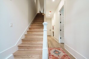 A staircase with wooden steps and white balusters, leading to a door with a decorative rug at the bottom. - Walk to Coffee and Food - 4 bedroom -2 Car Garage! (Nashville)