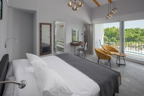 Quarto de hotel moderno com uma cama grande, uma escrivaninha, uma cadeira e uma varanda com vista.
