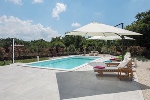 Piscina com espreguiçadeiras e guarda-sóis, cercada por um jardim bem cuidado.