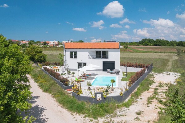 Uma casa moderna de dois andares com piscina, rodeada por um jardim bem cuidado e céu limpo.