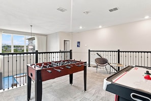 A room with a foosball table, a pool table, and a view of a residential area. - Perfect Family Escape, Pool, Themed Rooms (Kissimmee)