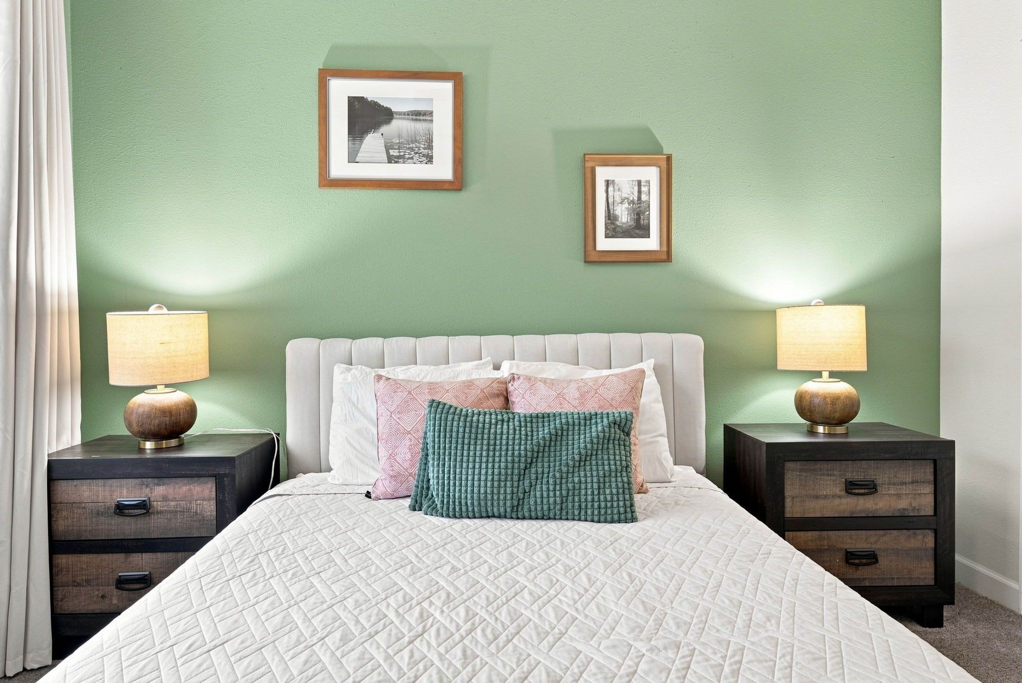 A bedroom with a bed, two nightstands, two wall-mounted lamps, and two framed pictures.