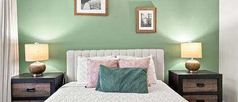 A bedroom with a bed, two nightstands, two wall-mounted lamps, and two framed pictures.