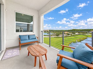 A balcony with a sofa, a table, and a view of a green landscape. - Lake View Family Escape, 2br, Close to Disney (Kissimmee)