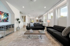 A modern living room with a black sofa, a coffee table, and a large painting on the wall. - Dream Family Escape, Pool and Themed Rooms (Clermont)