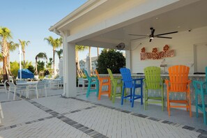 A covered outdoor seating area with colorful chairs and tables, a ceiling fan, and a sign that reads "RUMBRELAS". - Dream Family Escape, Pool and Themed Rooms (Clermont)