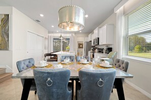 A modern dining area with a marble table, blue upholstered chairs, and a central hanging light fixture. - Dream Family Escape, Pool and Themed Rooms (Clermont)