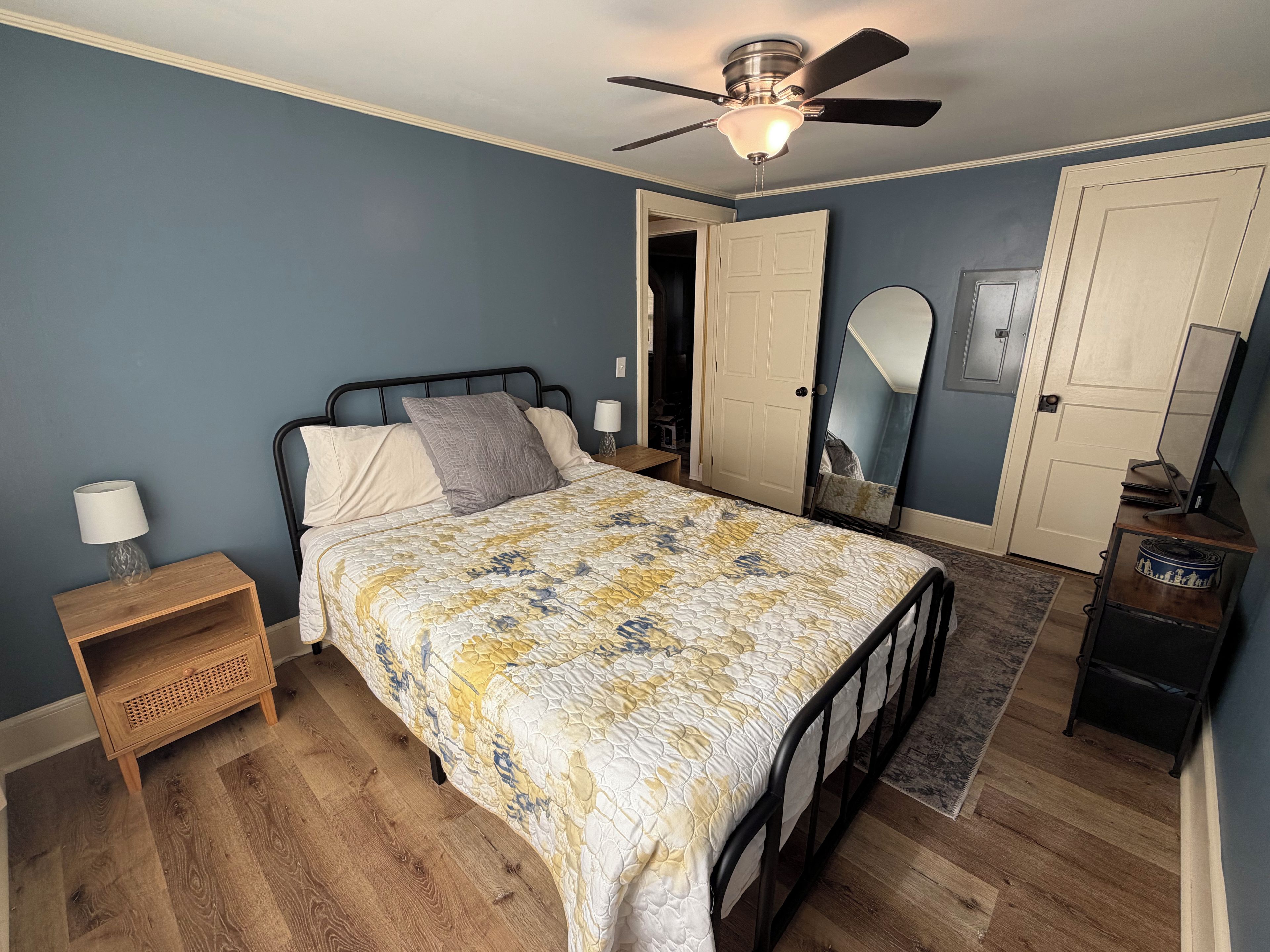 A bedroom with a bed, a nightstand, a dresser, a ceiling fan, and a door.