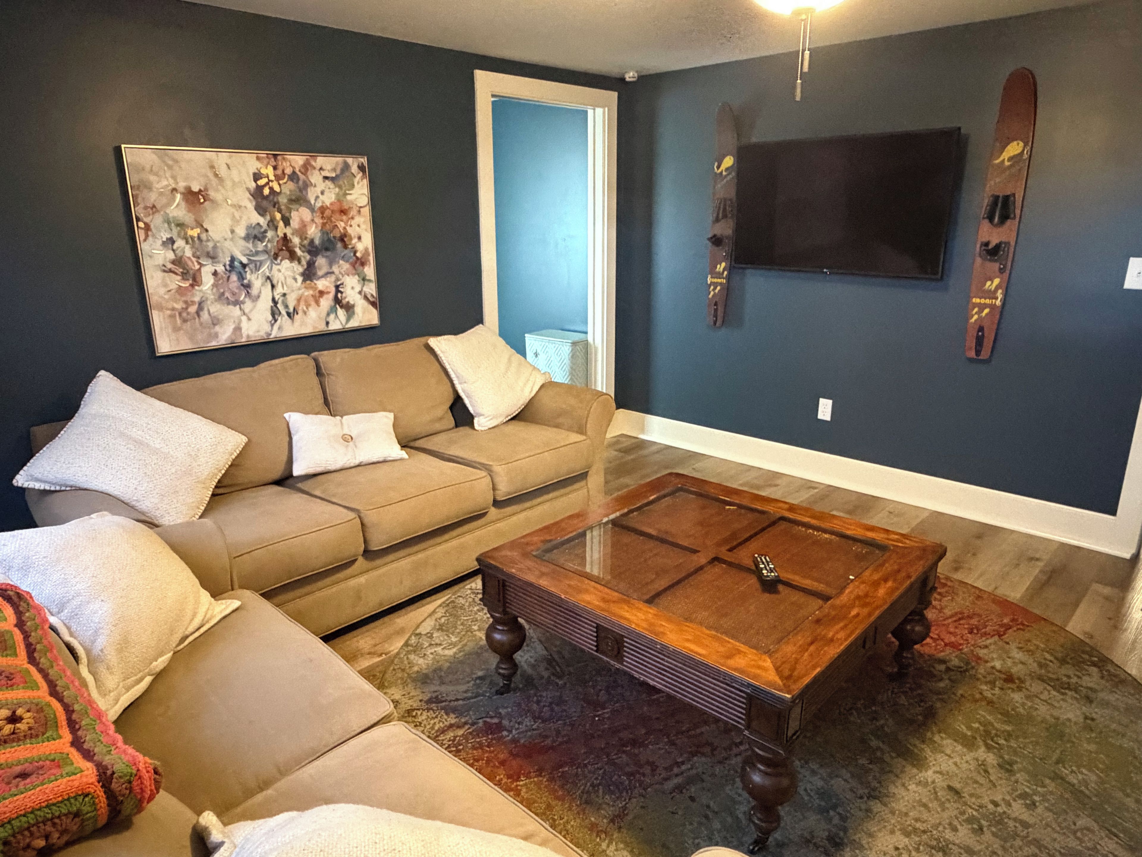 A living room with a sofa, coffee table, artwork, and skis mounted on the wall.