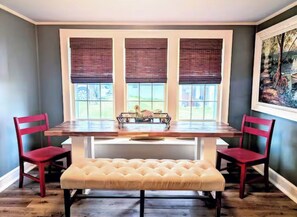A dining area with a wooden table, two red chairs, a bench, and a window with blinds. - Cozy Cottage Near Lake & Downtown Guntersville (Guntersville)