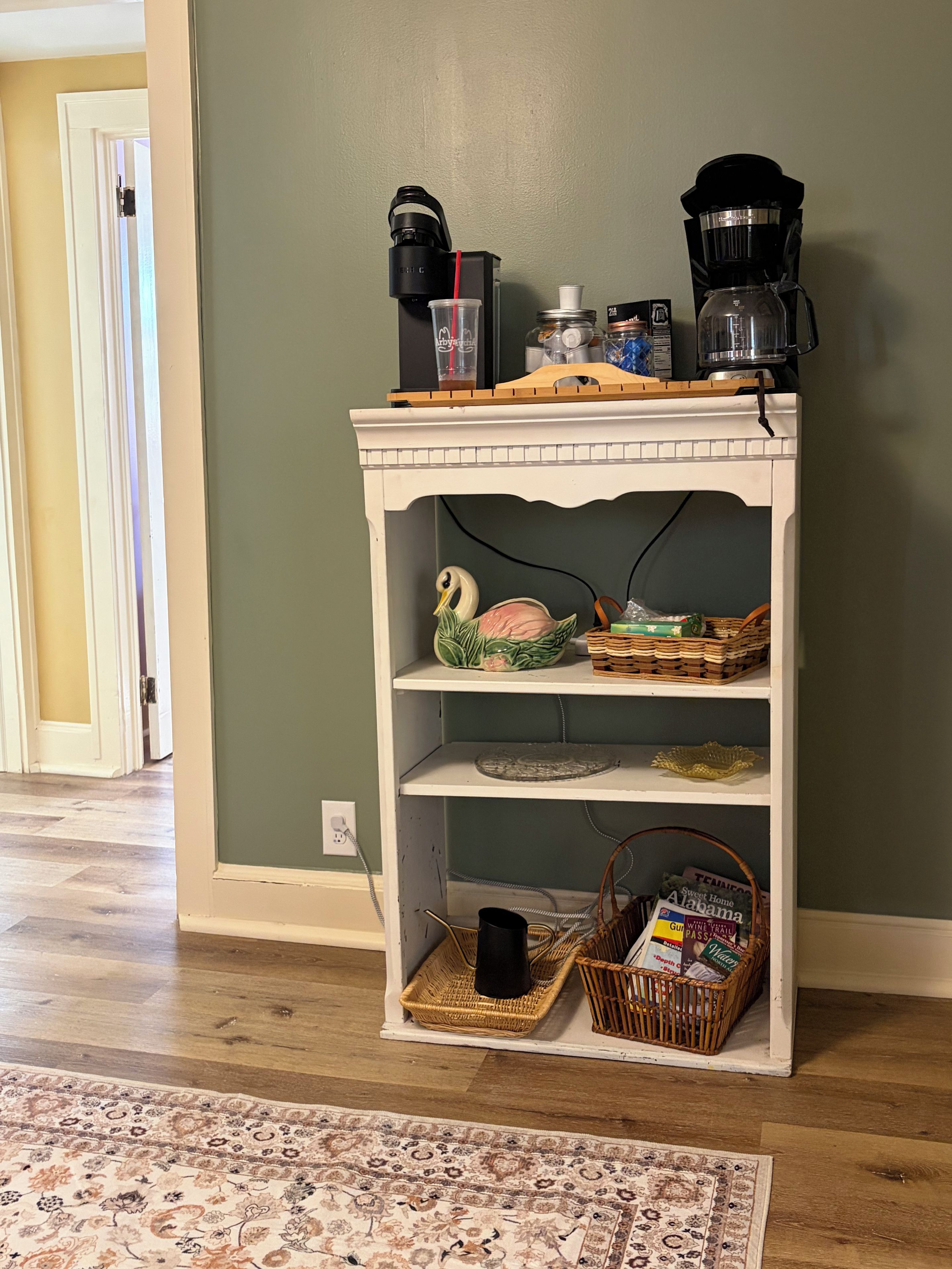 A white wooden shelf with various items including a coffee maker, a decorative bowl, and baskets.