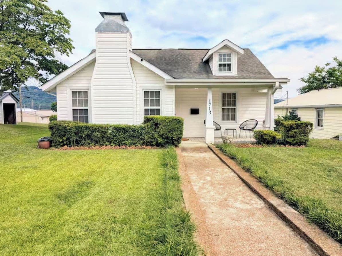 A single-story house with a front porch, a chimney, and a small garden area.
