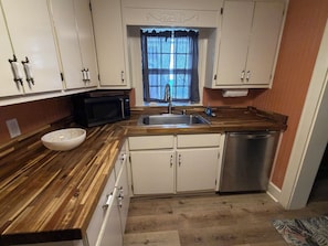 A kitchen with a wooden countertop, white cabinets, a stainless steel sink, a microwave, and a dishwasher. - Cozy Cottage Near Lake & Downtown Guntersville (Guntersville)