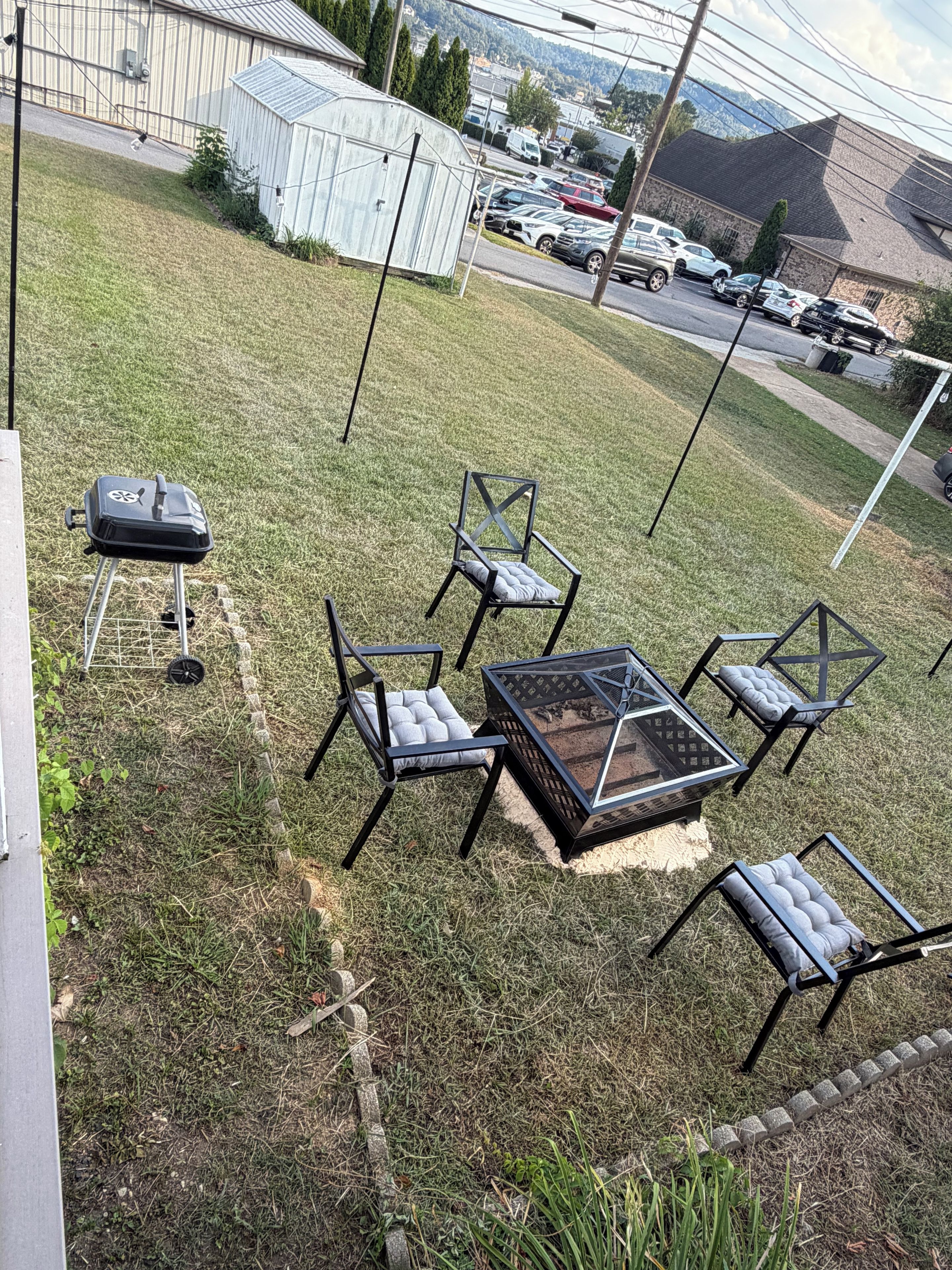 A patio area with outdoor furniture, a fire pit, and a view of a parking lot and buildings in the background.