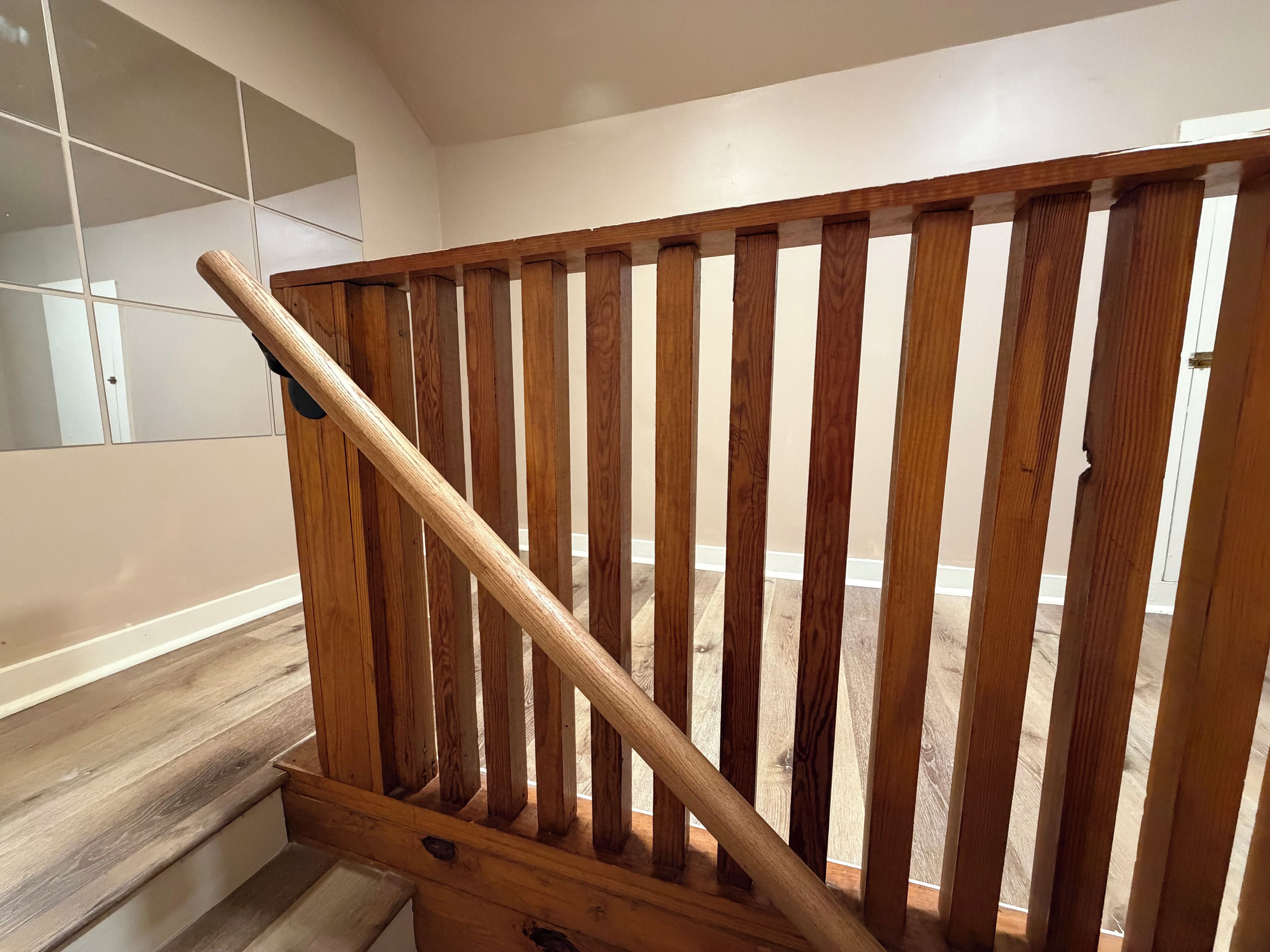 Eine hölzerne Treppe mit Handlauf, die zu einem Raum mit einer weißen Tür und einer gefliesten Wand führt.