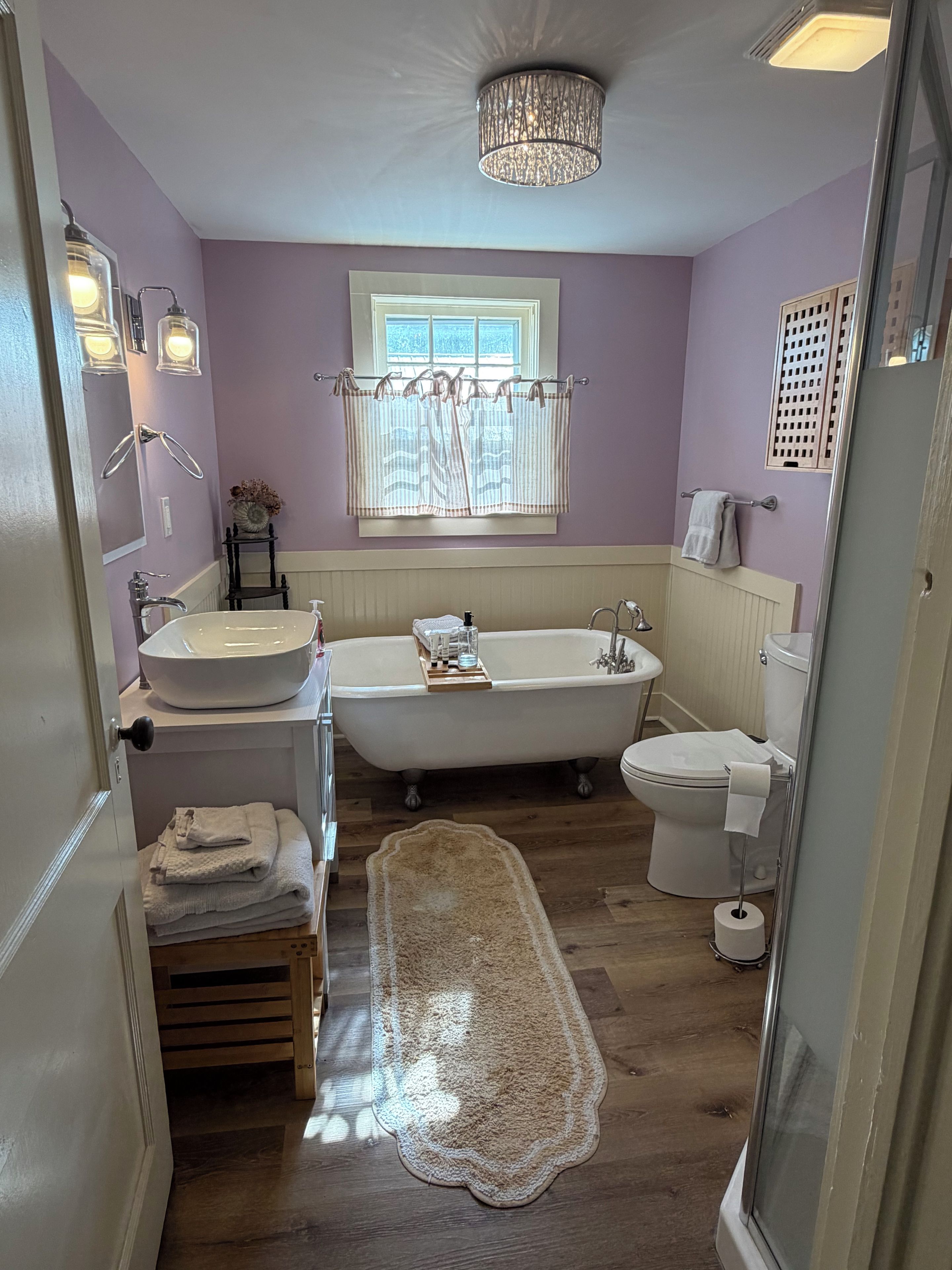 A bathroom with a freestanding bathtub, a toilet, a sink, and a window with curtains.