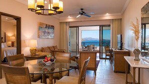 Una camera d'hotel con un balcone, un'area pranzo con un tavolo in vetro e vista sul mare.