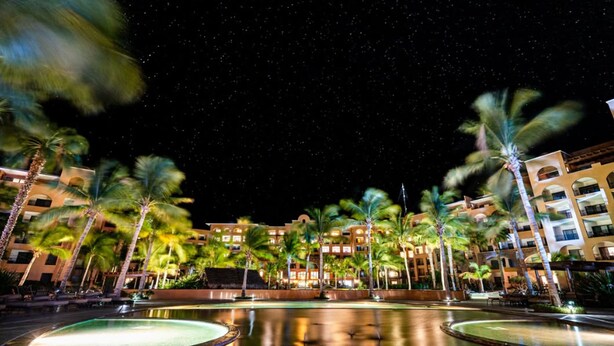 A hotel with multiple floors, palm trees, and a pool area at night. - Luxurious 1-bedroom 1 bath apartment in the heart of Loreto (Ensenada)