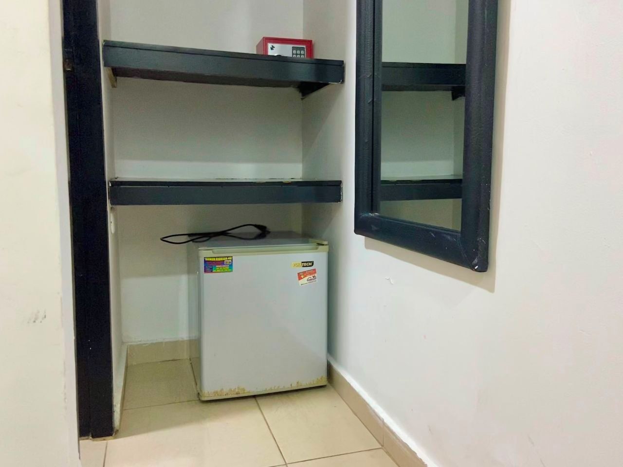 A small room with a white refrigerator, a black shelf, and a window with a black frame.