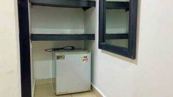 A small room with a white refrigerator, a black shelf, and a window with a black frame.