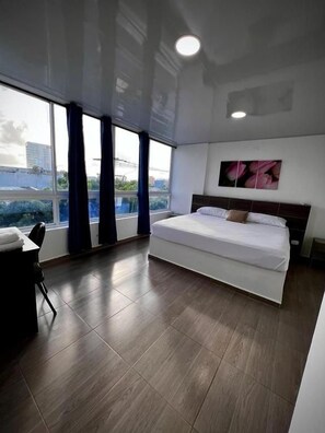A modern hotel room with a large bed, a desk, and a view through a window. - Hotel Sofichic by Caribecheap (Barranquilla)