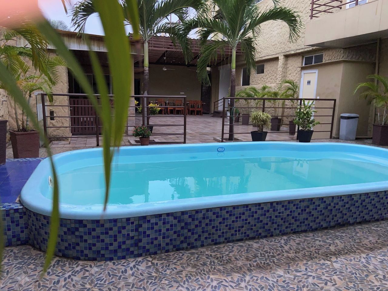 Piscina retangular com borda azulejada, rodeada por um terraço com mobiliário de exterior e plantas em vasos.