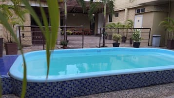 Piscina rectangular con borde de azulejos, rodeada por una terraza con mobiliario exterior y plantas en macetas.