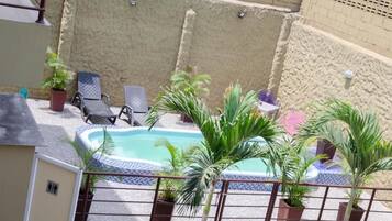 A rooftop pool area with lounge chairs, potted plants, and a small hot tub.