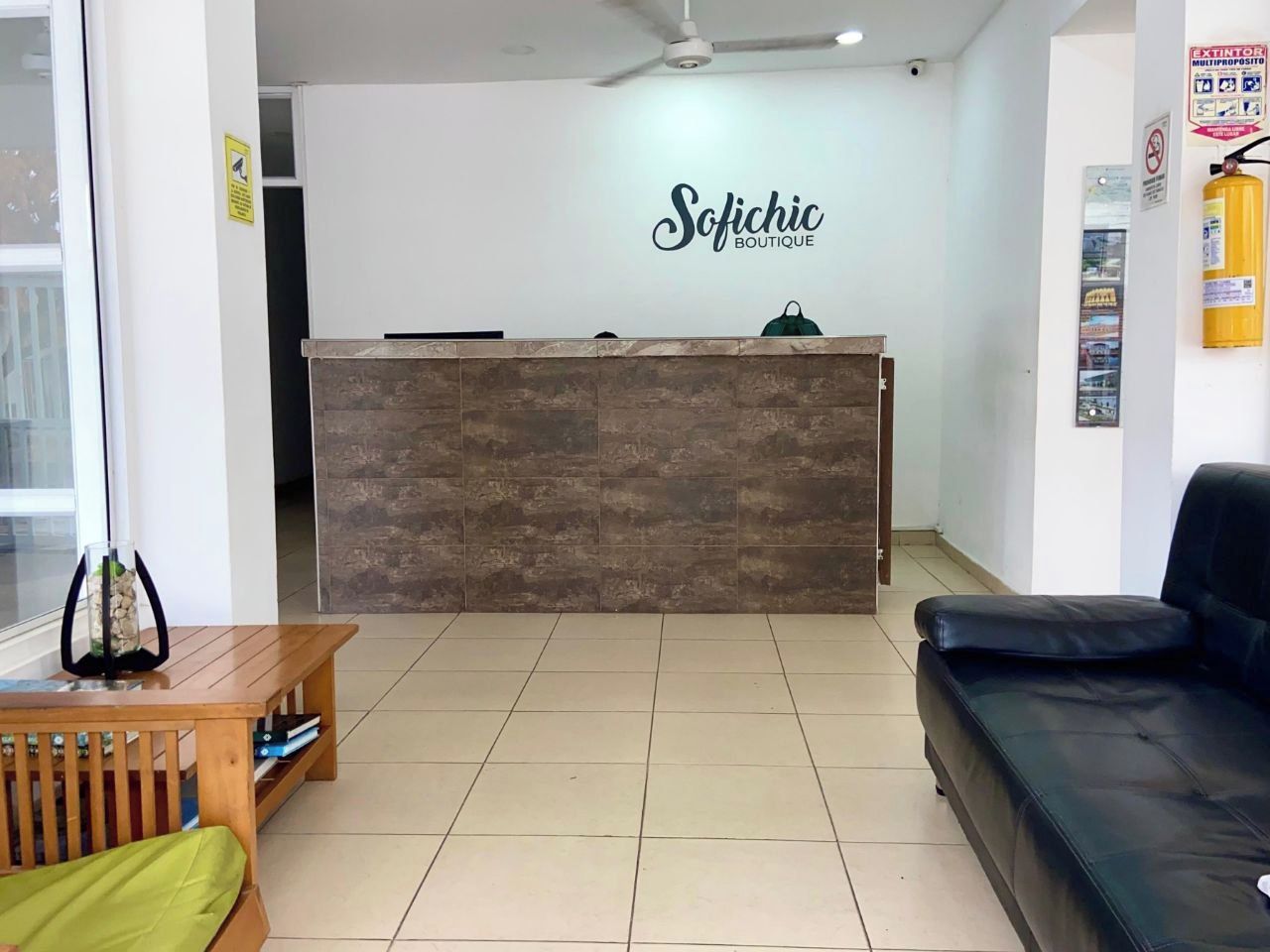 Un área de recepción con un mostrador de madera, un sofá de cuero negro y una pequeña mesa de madera con un cojín verde.