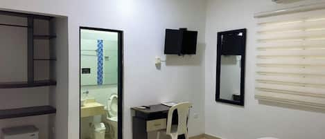 A hotel room with a bed, a desk, a chair, a TV, and a bathroom.