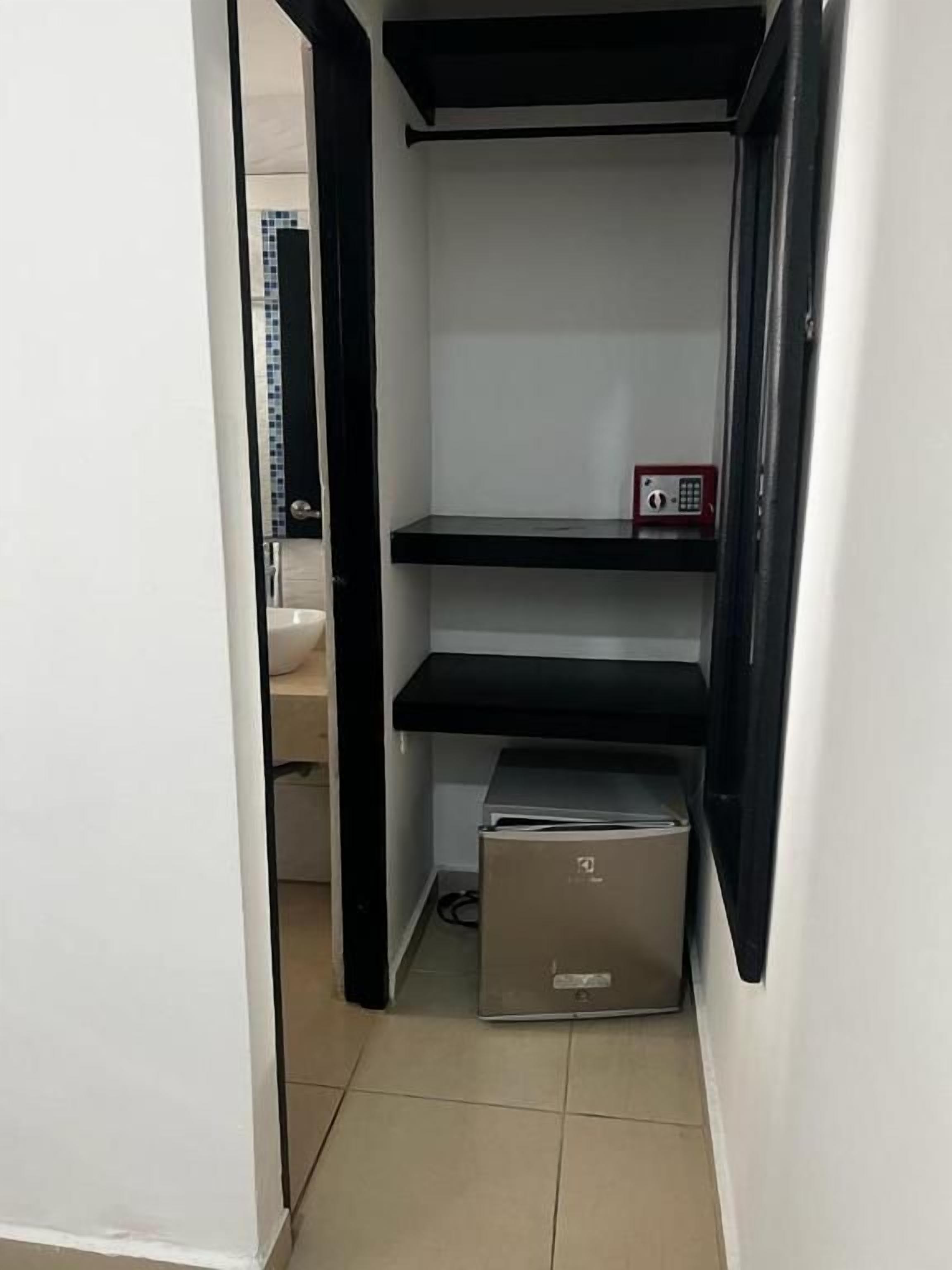 A narrow hallway with a black-framed shelf unit containing a small appliance, possibly a refrigerator, and a red emergency phone.
