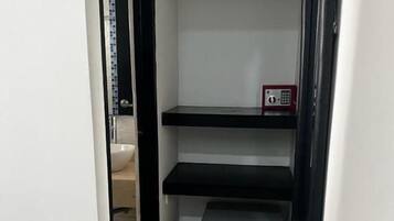 A narrow hallway with a black-framed shelf unit containing a small appliance, possibly a refrigerator, and a red emergency phone.