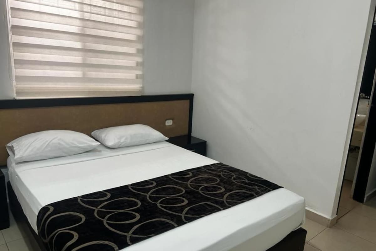 A single bed with a headboard, white bedding, and a black and gold patterned throw.