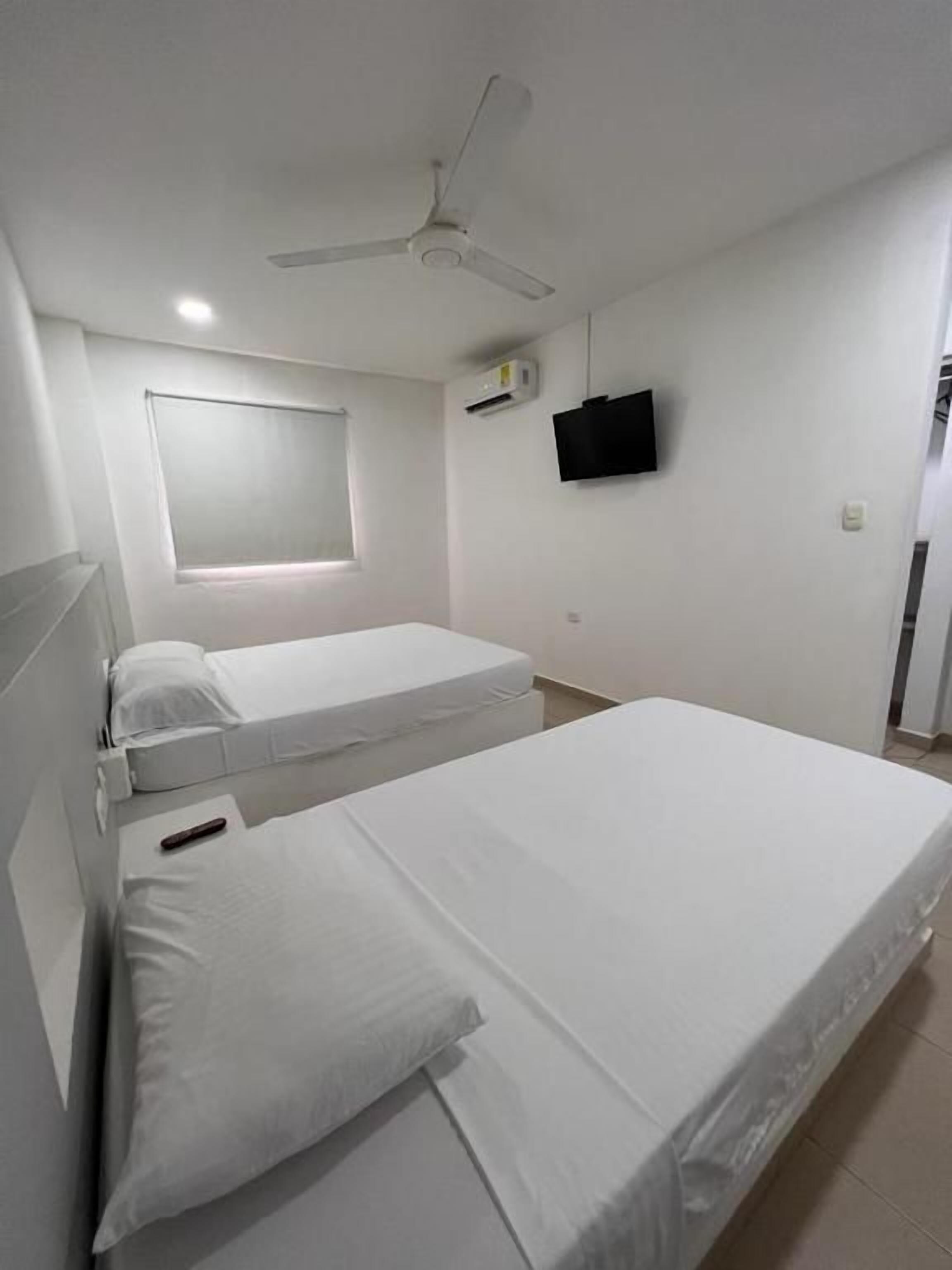 A hotel room with two beds, a ceiling fan, a mounted TV, and a window with blinds.