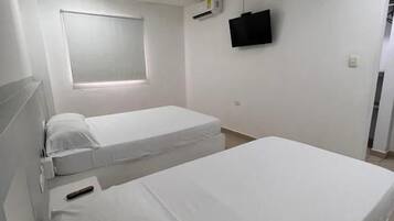 A hotel room with two beds, a ceiling fan, a mounted TV, and a window with blinds.